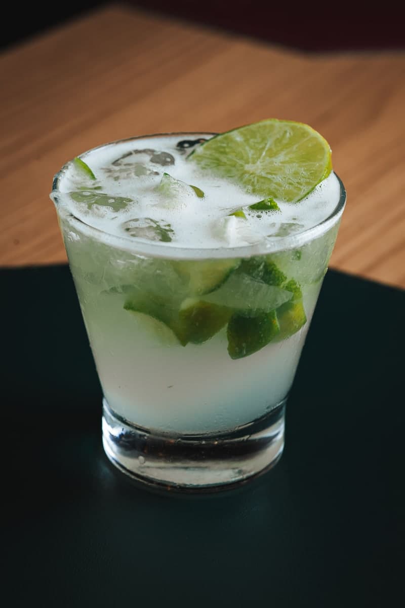 Caipirinha with muddled lime wedges and ice in a rocks glass, garnished with a lime slice