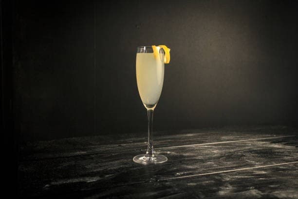 French 75-style sparkling cocktail in a flute with a lemon peel garnish on a black tabletop
