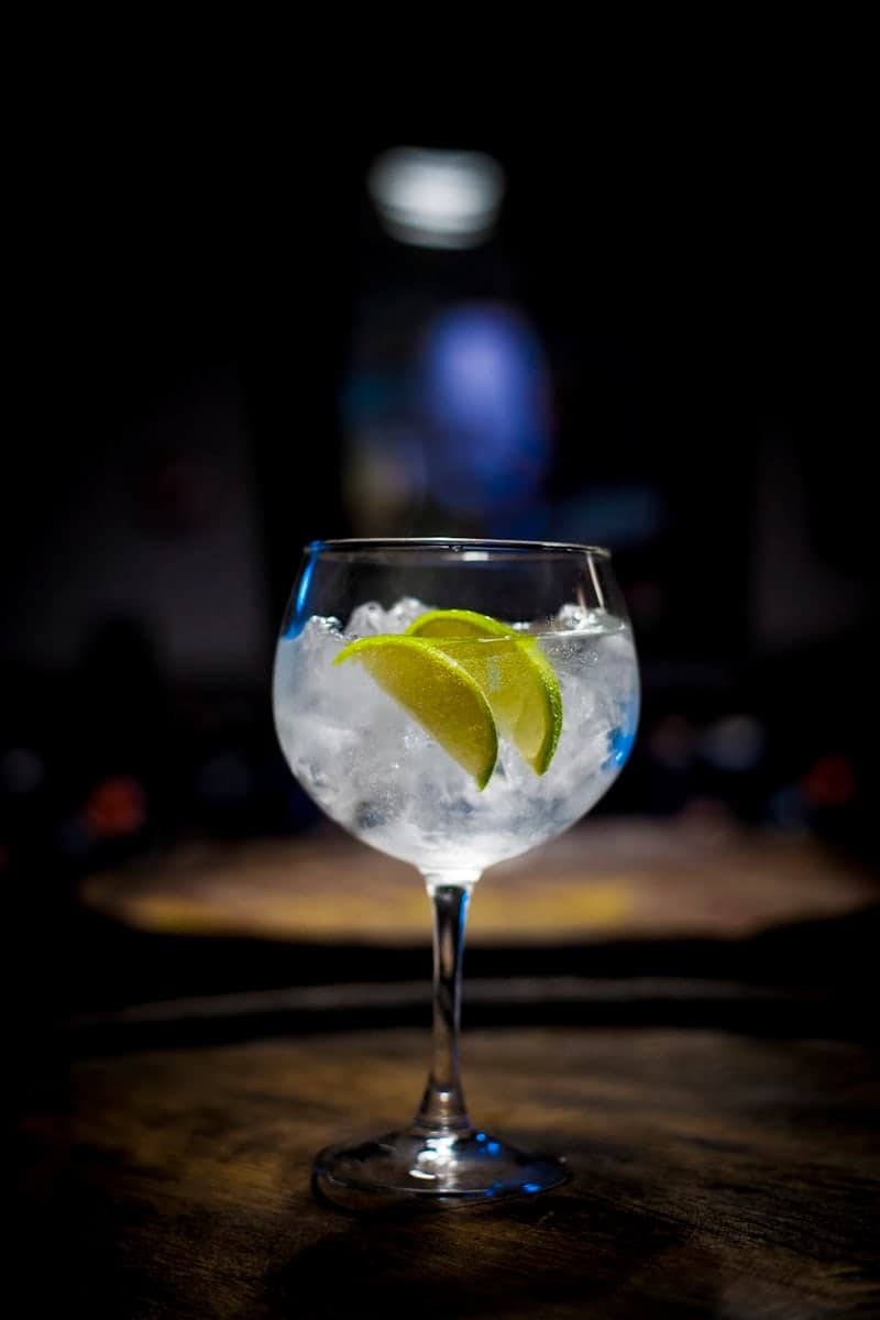 Gin and Tonic in a stemmed copa glass with fresh ice and lime wedges on a dark wooden surface