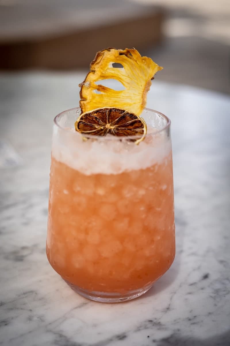 Orange Mai Tai-style cocktail in a rocks glass with crushed ice, dried citrus, and pineapple garnish on a marble counter