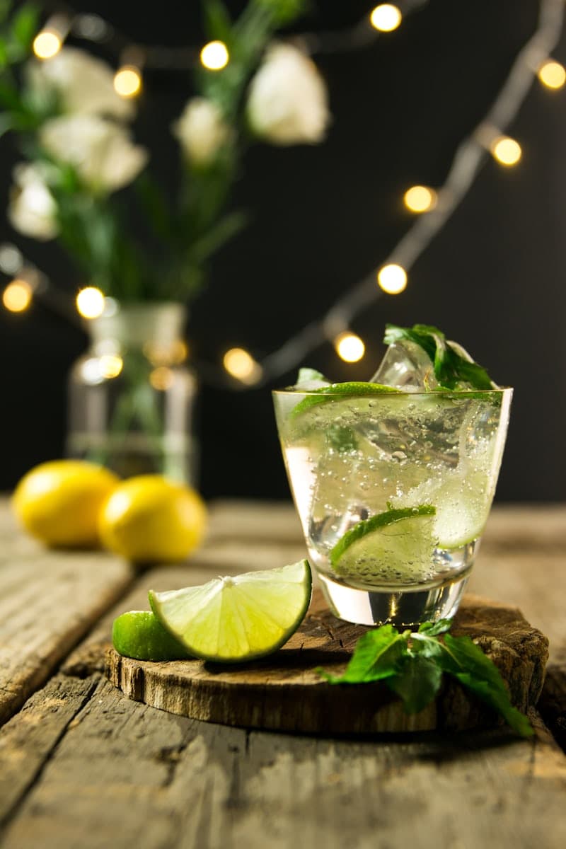Mojito with lime and mint on a wooden surface with warm lights behind it