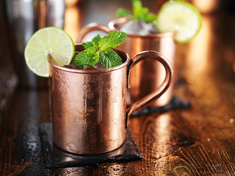 Moscow Mule-style highballs in copper mugs with fresh ice, lime wheels, and mint garnish on a wet wooden surface