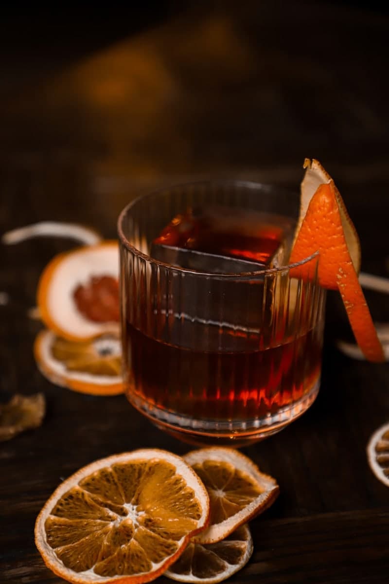 Red Negroni in a ribbed rocks glass with a large ice cube, orange peel garnish, and dried citrus slices