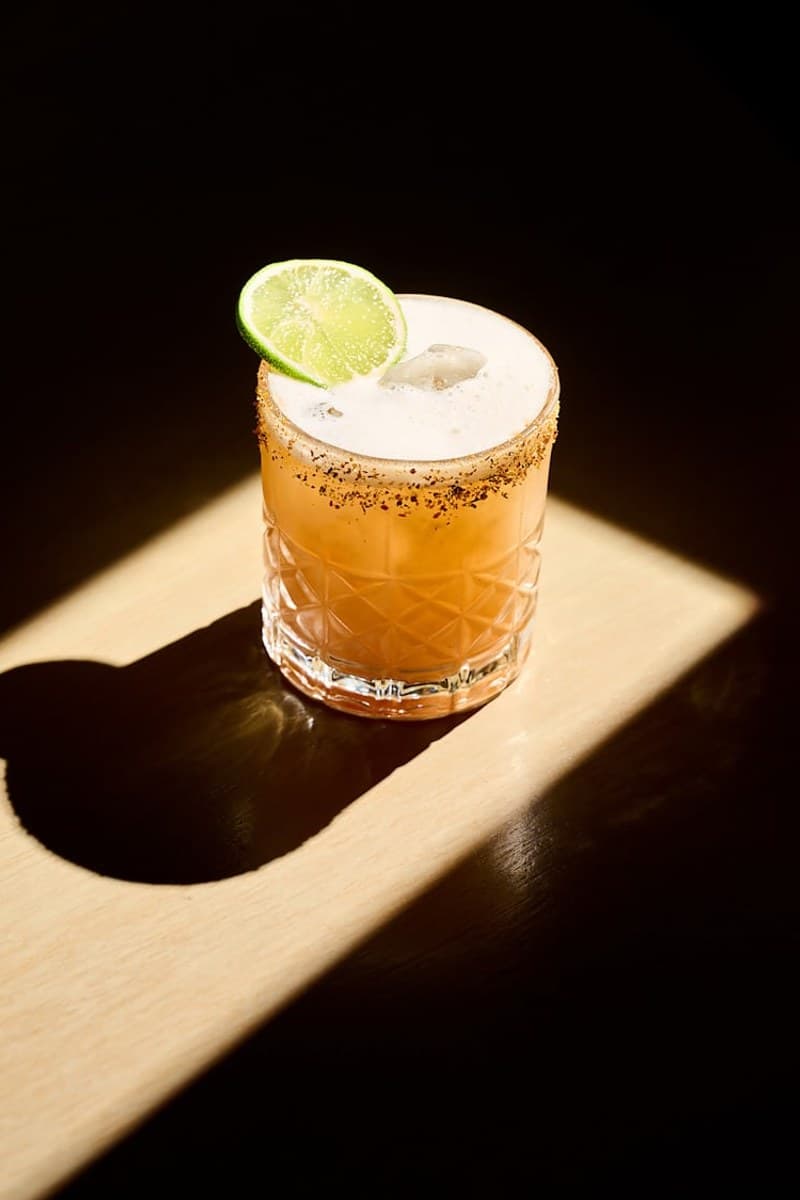 Grapefruit-colored Paloma with fresh ice, a salt-and-spice rim, and a green citrus wheel garnish